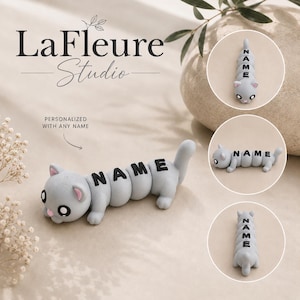 May include: A gray, segmented cat-shaped figurine with large black eyes and pink inner ears. The body consists of rounded sections, each featuring a black letter forming the word NAME. The figurine is shown from multiple angles.