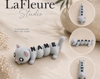 May include: A gray, segmented cat-shaped figurine with large black eyes and pink inner ears. The body consists of rounded sections, each featuring a black letter forming the word NAME. The figurine is shown from multiple angles.