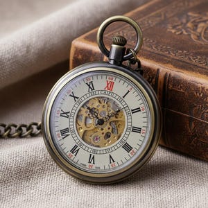 Op de afbeelding: Antieke zakhorloge met een bronzen behuizing en ketting. De wijzerplaat toont Romeinse cijfers, zichtbare tandwielen en de tekst "CAIFU". Het ligt op een neutrale stof, met een leren boek op de achtergrond.