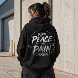 Pode incluir: Moletom preto com a frase "FIND PEACE THROUGH THE PAIN" em branco. O design está nas costas. O moletom tem capuz com cordão e um ajuste solto.