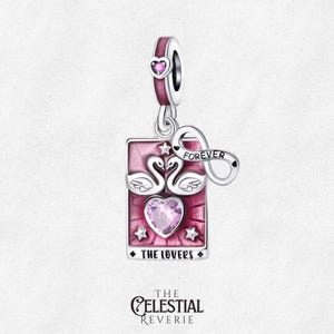 May include: A silver charm with a pink rectangular pendant featuring two swans, a heart, and stars. The charm includes an infinity symbol with the word "FOREVER" and a small heart. The text "THE LOVERS" is at the bottom.