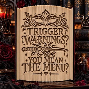 Könnte beinhalten: Eine Buchfaltkunst-Skulptur mit dem Text TRIGGER WARNINGS? YOU MEAN THE MENU?, der in die Seiten eingearbeitet ist. Das Design zeigt eine Maskenballmaske, einen Dolch und Rosen. Die cremefarbenen Seiten sind gefaltet, um einen 3D-Effekt zu erzielen.
