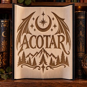 May include: A book art sculpture featuring the text ACOTAR folded into the pages. The design includes a crescent moon, a central star, stylized wings, and a mountain range with pine trees at the base, all created through precise page folding.