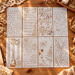 May include: A set of eight rectangular white plastic stencils featuring various cut-out designs including a stone wall pattern, musical notes, alphabet letters, numbers, vintage script text, a guitar, a compass, and bare tree branches.