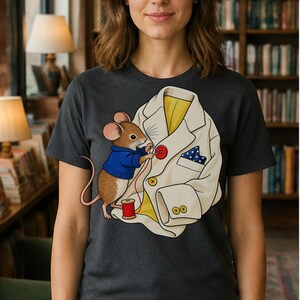 Könnte beinhalten: Ein anthrazitfarbenes T-Shirt mit einer grafischen Illustration einer braunen Maus in einem blauen Pullover. Die Maus näht einen roten Knopf an einen cremefarbenen Blazer mit gelbem Innenfutter, blau-weiß gepunktetem Einstecktuch und Knöpfen.