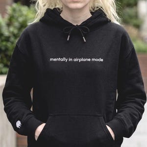 Puede incluir: Sudadera negra con el texto blanco "mentally in airplane mode". La sudadera tiene una capucha con cord&oacute;n y un bolsillo delantero. Un peque&ntilde;o dise&ntilde;o blanco es visible en la manga izquierda.