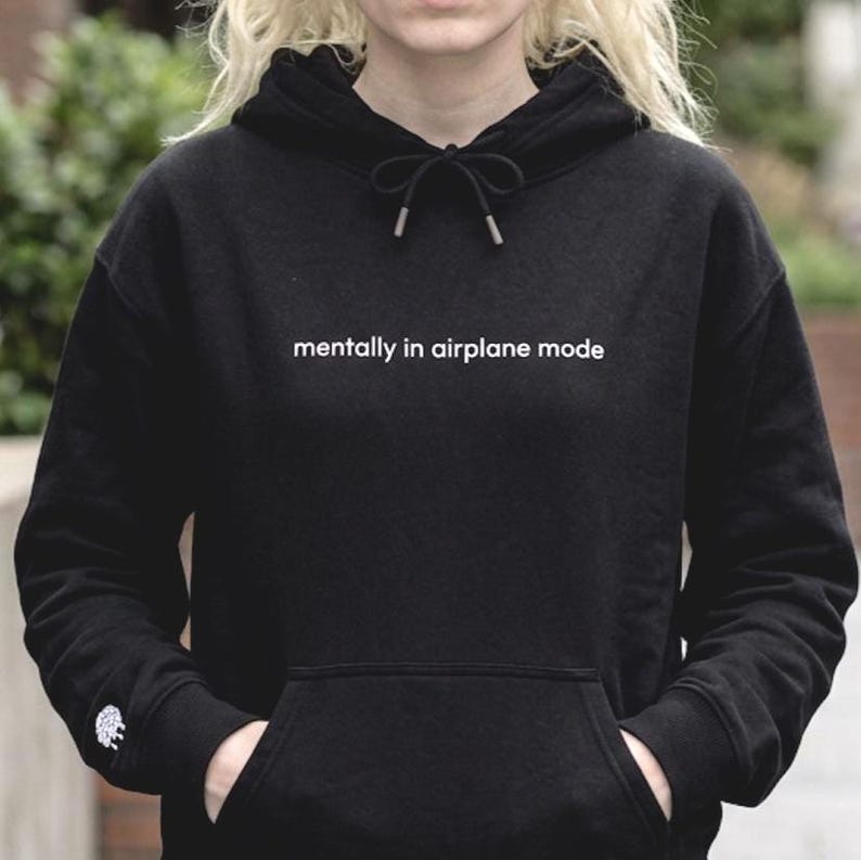 Puede incluir: Sudadera negra con el texto blanco "mentally in airplane mode". La sudadera tiene una capucha con cord&oacute;n y un bolsillo delantero. Un peque&ntilde;o dise&ntilde;o blanco es visible en la manga izquierda.