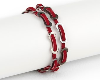 May include: A red leather bracelet with silver and gray metal chain links. The bracelet is rolled up on a white surface.