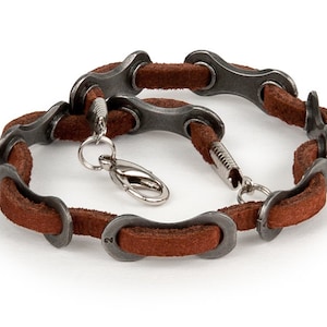 May include: A brown leather bracelet with silver metal bike chain links. The bracelet has a silver clasp.