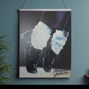 May include: A framed print featuring a black and white image of Michael Jackson's feet in black shoes and white socks. The image is signed "Michael Jackson" in cursive. The print is displayed on a wall.