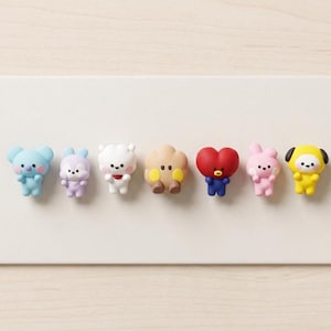 May include: A row of seven colorful cartoon character figurines. The characters include a light blue koala, a purple bunny, a white sheep, a tan cloud, a red heart, a pink bunny, and a yellow dog. Each figurine has a unique design.