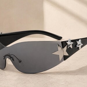 May include: Black sunglasses with a wraparound design and gray lenses. The sunglasses feature silver star accents on the temples. A stylish accessory for eye protection.