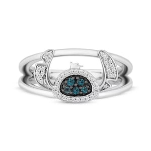 Op de afbeelding: Een zilveren ring met een centraal cluster van blauwe edelstenen, omringd door een halo van witte edelstenen. De ring heeft een unieke vorm met gebogen accenten en extra witte edelstenen.