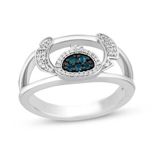 Op de afbeelding: Een zilveren ring met een centraal ontwerp van blauwe edelstenen in een zwarte rand, omringd door witte edelstenen. De ring heeft een gespleten schachtontwerp. Dit sieraad is een decoratief accessoire.