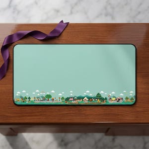 May include: A rectangular mouse mat with a light teal background and a colourful illustrated border depicting a campsite scene with trees, tents, and vehicles. A purple ribbon is draped across the top.
