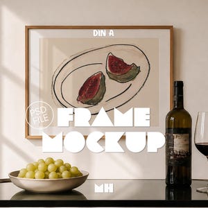 May include: A rectangular wooden frame containing a print of two watermelon slices on a plate. The text DIN A, PSD FILE, FRAME MOCKUP, and MH are overlaid. A bowl of green grapes, a wine bottle, and a wine glass are positioned in front.