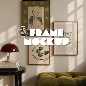 May include: Three rectangular wall frames in black and wood tones, displaying art prints of two cranes, a bowl of olives, and a botanical sketch. The frames are arranged on a wall above a green tufted sofa and a side table with a dark red lamp.