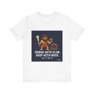 May include: White t-shirt featuring a pixelated caveman holding a club and a rock. The design includes the text "DEBUG WITH CLUB. SHIP WITH ROCK. LET IT BE IT" in white, with a dark blue background.