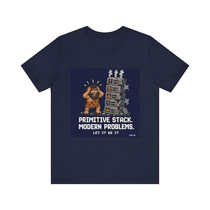 Op de afbeelding: Marineblauw T-shirt met een pixelafbeelding van een holbewoner en een stapel stenen blokken. De tekst luidt: "PRIMITIVE STACK. MODERN PROBLEMS. LET IT BE IT."
