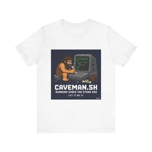 May include: White t-shirt featuring a graphic of a caveman using a stone-age computer. The design includes the text "CAVEMAN.SH RUNNING SINCE THE STONE AGE LET IT BE IT". A humorous design for tech enthusiasts.