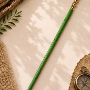 May include: A long walking stick featuring a textured green shaft with a mottled finish, divided into three segments by thin gold-coloured metal rings. The handle is a polished gold-coloured metal knob with a tiered, rounded design.