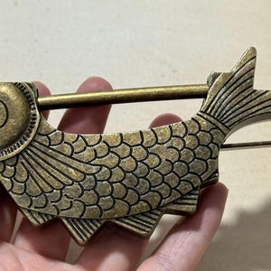 May include: A decorative fish-shaped lock with an antique brass finish. The lock features detailed scales, fins, and a tail, with a sliding bar for securing. The design is reminiscent of vintage or Asian-inspired decor.