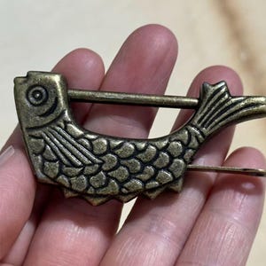 Puede incluir: Un candado en forma de pez de estilo vintage, con acabado en bronce. El candado presenta escamas, aletas y un ojo detallados, con una barra deslizante para asegurar. Una pieza decorativa única.