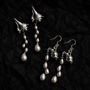 May include: Two pairs of silver-toned drop earrings. One pair features textured seashell charms with dangling white teardrop pearls. The second pair features small silver-toned pitcher charms with dangling white teardrop pearls on thin metal chains.