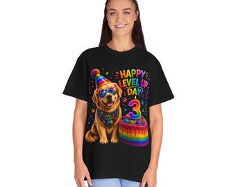 Puede incluir: Una camiseta negra con un gráfico de un golden retriever con un sombrero de fiesta y gafas de sol arcoíris, un pañuelo que dice LEVEL 3 UNLOCKED y un pastel de cumpleaños arcoíris con una vela del número 3, con el texto HAPPY LEVEL UP DAY.
