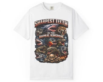 Puede incluir: Una camiseta blanca de manga corta con un estampado gráfico de varios animales depredadores con los dientes al descubierto, incluyendo un tiburón, un lobo y un tigre. El texto "SHARPEST TEETH IN THE ANIMAL KINGDOM" aparece sobre los animales.