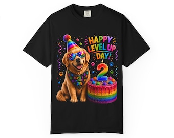 Puede incluir: Una camiseta negra con un golden retriever que lleva un gorro de fiesta arcoíris, gafas de sol y un pañuelo que dice LEVEL 2 UNLOCKED. Junto al perro hay un pastel de cumpleaños arcoíris con una vela del número 2 y el texto HAPPY LEVEL UP DAY.