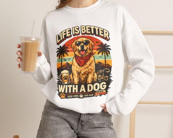 Puede incluir: Una sudadera blanca de manga larga con un gráfico de un golden retriever con gafas de sol y un pañuelo rojo. El diseño incluye palmeras, una jarra de cerveza, una furgoneta y el texto "LIFE IS BETTER WITH A DOG" y "GOOD VIBES DOG HAIR".
