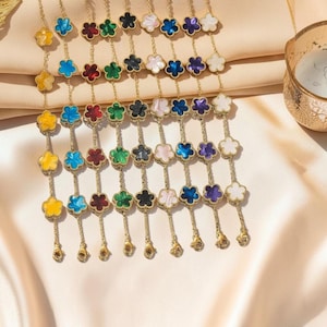 May include: A selection of gold-coloured necklaces featuring flower-shaped pendants in a variety of colours, such as yellow, blue, red, green, black, pink, and white. The pendants are linked by fine chains.