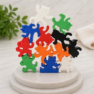 May include: A wooden cat stacking toy in a variety of colours. The cats are white, green, blue, red, orange, and black. The cats are stacked on a white, round, tiered base. The toy is designed for play and display.