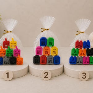 May include: Three sets of colourful, miniature toy trucks are displayed in clear cellophane bags tied with gold ribbon. Each set is arranged on a white pedestal with a numbered wooden disc in front.