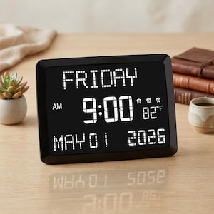 May include: A black digital clock displaying "FRIDAY", "9:00 AM", "MAY 01 2026", and 82°F. The clock has a rectangular shape and is set on a wooden surface.