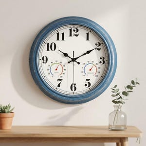 May include: A round wall clock with a distressed blue frame and a white face featuring large black Arabic numerals. The clock includes two smaller circular analog gauges at the bottom, one for humidity and one for temperature in Fahrenheit.