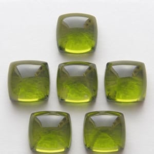 May include: Six square-shaped, translucent olive green cabochons with rounded corners and a smooth, polished surface. The stones are arranged in a symmetrical pattern, featuring a glossy finish that reflects light across their curved tops.