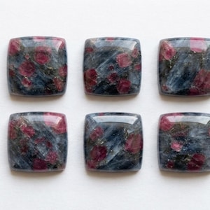 Puede incluir: Seis cabujones cuadrados con esquinas redondeadas, con una superficie pulida de matriz de piedra azul oscuro y gris con inclusiones circulares de color rosa vibrante y rojo, dispuestos en dos filas de tres sobre un fondo blanco.