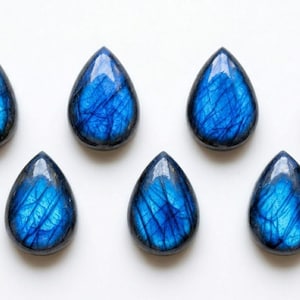 May include: Seven teardrop-shaped labradorite gemstones arranged in two rows. Each stone features a polished, smooth surface with a vibrant, iridescent blue flash and visible internal fractures that create a distinct, web-like pattern throughout.