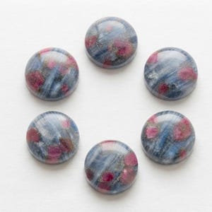 Könnte beinhalten: Sechs kreisförmige Cabochons, die in einer Ringform angeordnet sind. Jedes Stück hat eine polierte, glatte Oberfläche mit einem ausgeprägten Muster aus dunkelblauen, grauen und weißen Streifen, durchsetzt mit leuchtenden, runden magenta- und dunkelrosafarbenen Einschlüssen.
