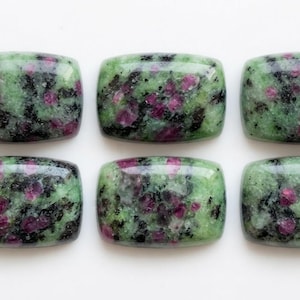 Puede incluir: Seis cabujones rectangulares de zoisita pulida con inclusiones de rubí. Cada piedra presenta una superficie lisa y redondeada con un patrón moteado de depósitos minerales en verde claro, magenta intenso y negro en dos filas.