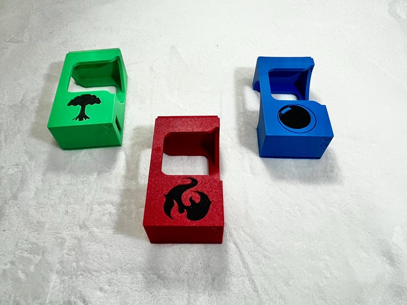 May include: Three colorful, geometric card holders. One is green with a black tree design, another is red with a black flame design, and the third is blue with a black circle. The holders are made of a solid material.