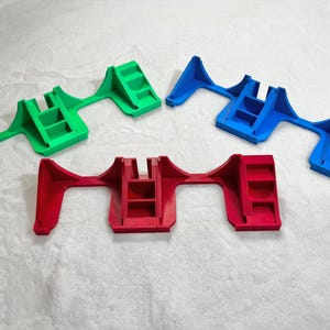 May include: Four plastic, multi-colored objects. The objects are in green, blue, and red. Each object has a unique shape with a series of steps and a central support structure. The objects are likely for supporting or holding other items.