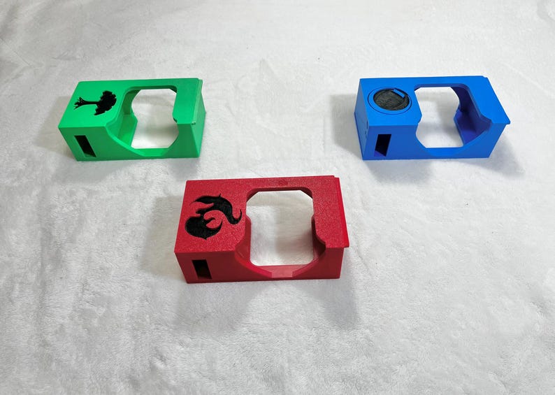 May include: Three colorful, rectangular cases with cut-out sections. One is green with a tree silhouette, another is red with a black flame design, and the third is blue with a circular detail.