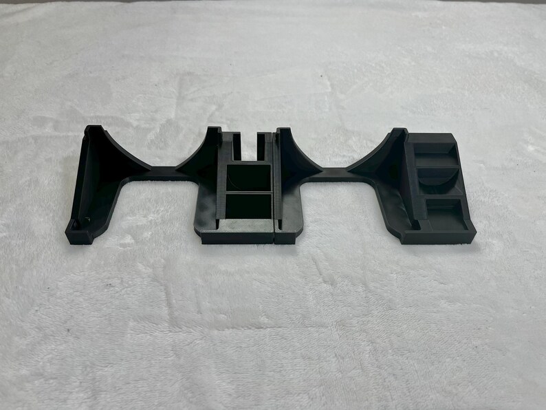 May include: A black plastic bracket with a unique shape, featuring a central rectangular section and curved, flared ends. The bracket has a series of rectangular cutouts and raised sections, suggesting a structural or mounting component.