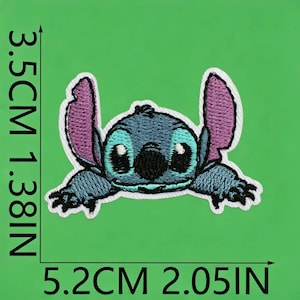 Op de afbeelding: Een geborduurde patch van het blauwe buitenaardse personage Stitch met grote paarse oren, zwarte ogen en een zwarte neus. De patch meet 3,5 cm bij 5,2 cm, zoals aangegeven door de zwarte meetlijnen op de afbeelding.