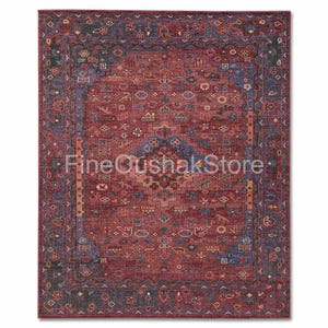 Puede incluir: Una alfombra rectangular con un campo central rojo intenso, adornada con intrincados motivos geométricos y florales en tonos azules, dorados y verdes. La alfombra presenta un borde detallado y el texto "FineOushakStore".