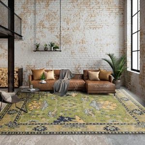 May include: A living room scene featuring a large, patterned rug in shades of green, blue, and yellow. A brown leather sofa with throw pillows and a gray blanket sits atop the rug. The room has a brick wall and a large window.