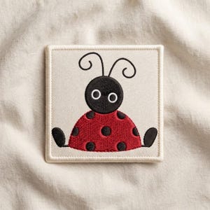 May include: A square patch featuring an embroidered ladybug design on a cream-colored fabric base. The ladybug has a black head with two white circular eyes, two antennae, a red body with black spots, and two black oval-shaped feet.